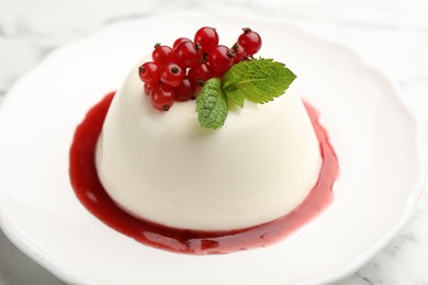 Photo of Delicious panna cotta with red currants, sauce and mint on white marble table, closeup