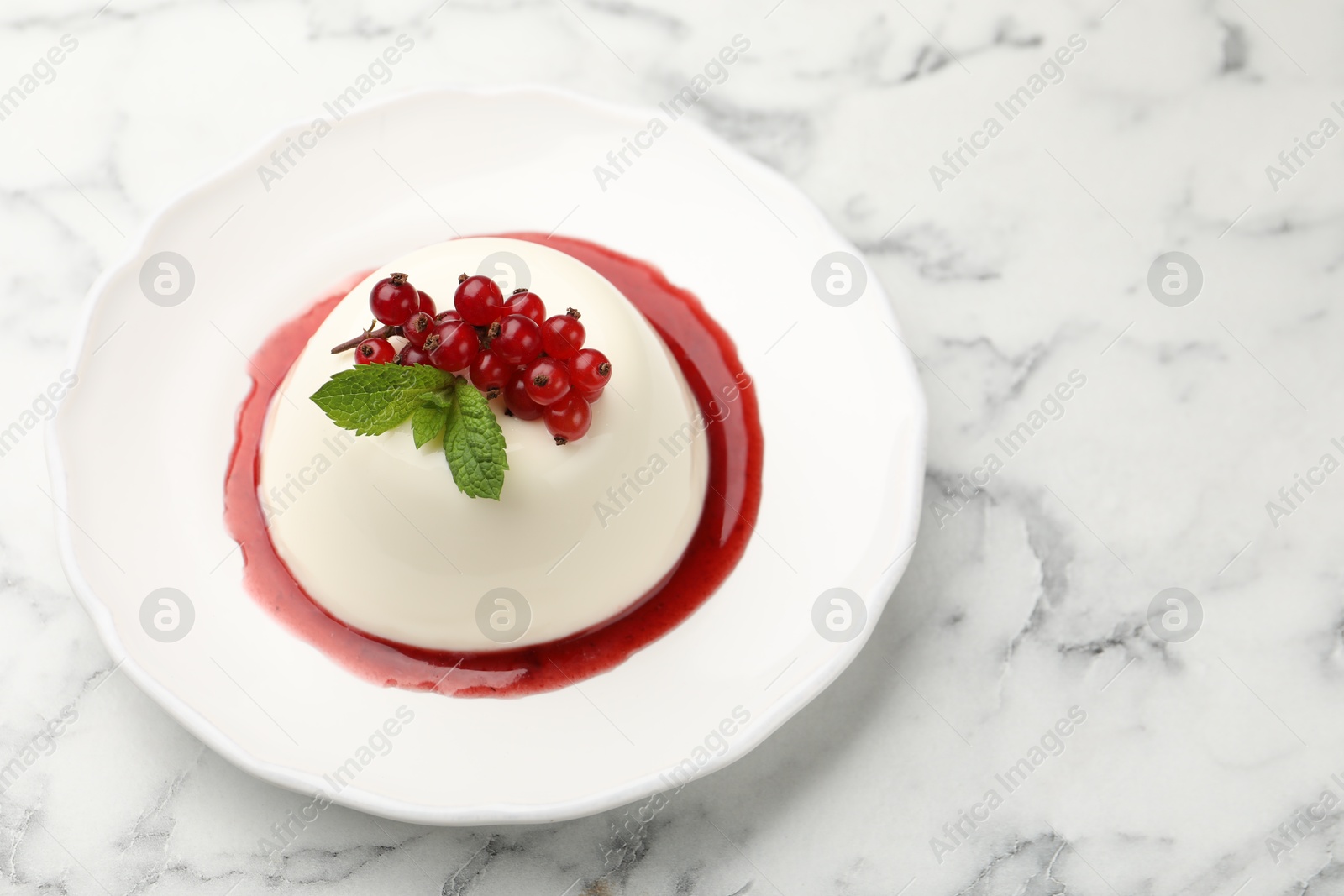 Photo of Delicious panna cotta with red currants, sauce and mint on white marble table