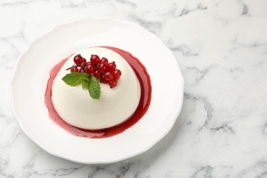 Photo of Delicious panna cotta with red currants, sauce and mint on white marble table
