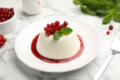 Photo of Delicious panna cotta with red currants, sauce and mint on white marble table, closeup