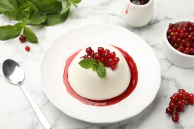 Photo of Delicious panna cotta with red currants, sauce and mint on white marble table, closeup