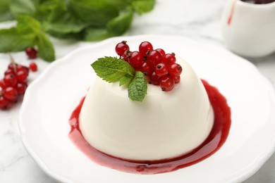 Photo of Delicious panna cotta with red currants, sauce and mint on white marble table, closeup