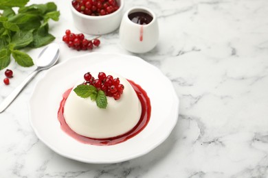 Photo of Delicious panna cotta with red currants, sauce and mint on white marble table, closeup