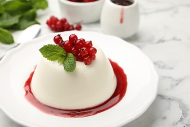 Photo of Delicious panna cotta with red currants, sauce and mint on white marble table, closeup