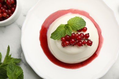 Photo of Delicious panna cotta with red currants, sauce and mint on white marble table, flat lay