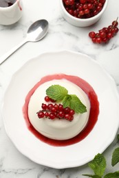 Photo of Delicious panna cotta with red currants, sauce and mint on white marble table, flat lay