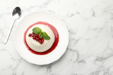 Photo of Delicious panna cotta with red currants, sauce, mint and spoon on white marble table, flat lay. Space for text
