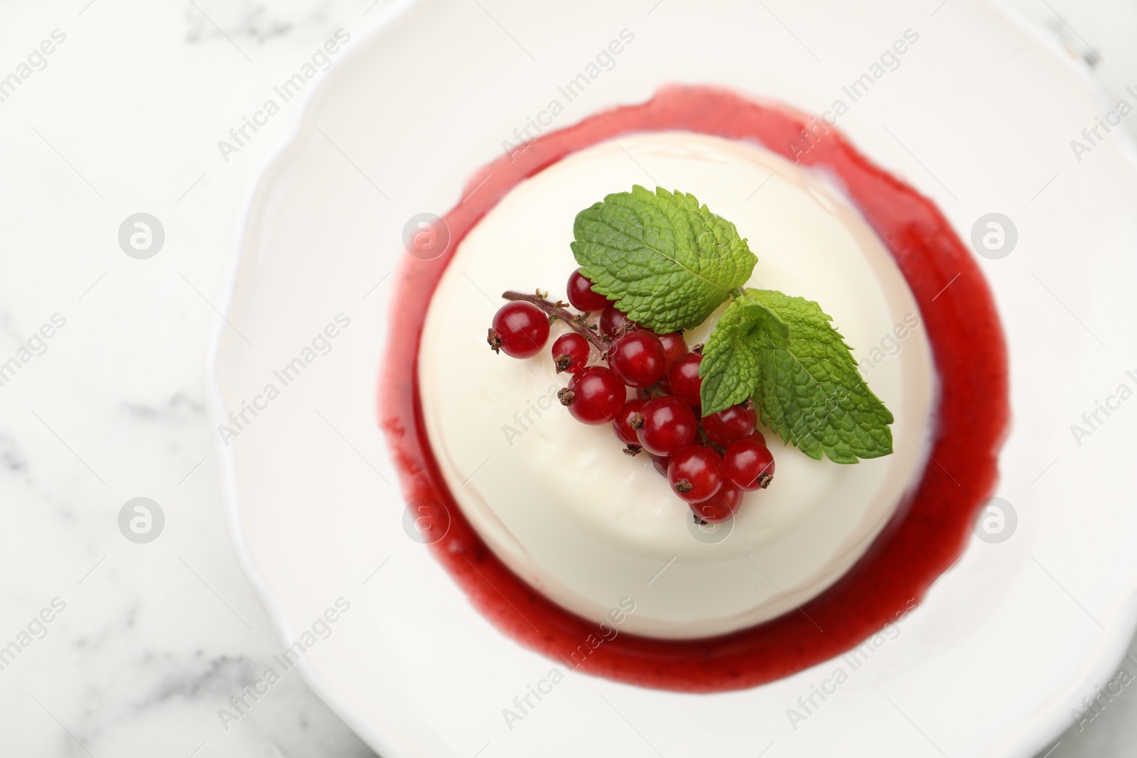 Photo of Delicious panna cotta with red currants, sauce and mint on white marble table, top view