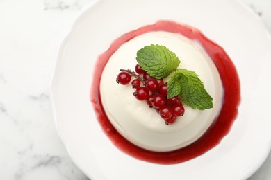 Photo of Delicious panna cotta with red currants, sauce and mint on white marble table, top view