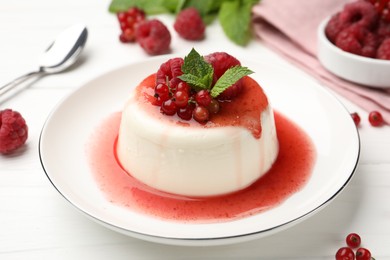 Photo of Delicious panna cotta with berries, sauce and mint on white wooden table, closeup