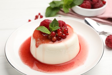 Photo of Delicious panna cotta with berries, sauce and mint on white wooden table, closeup