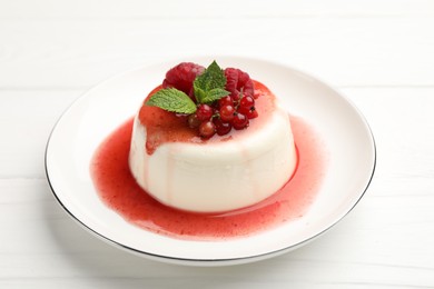 Photo of Delicious panna cotta with berries, sauce and mint on white wooden table, closeup