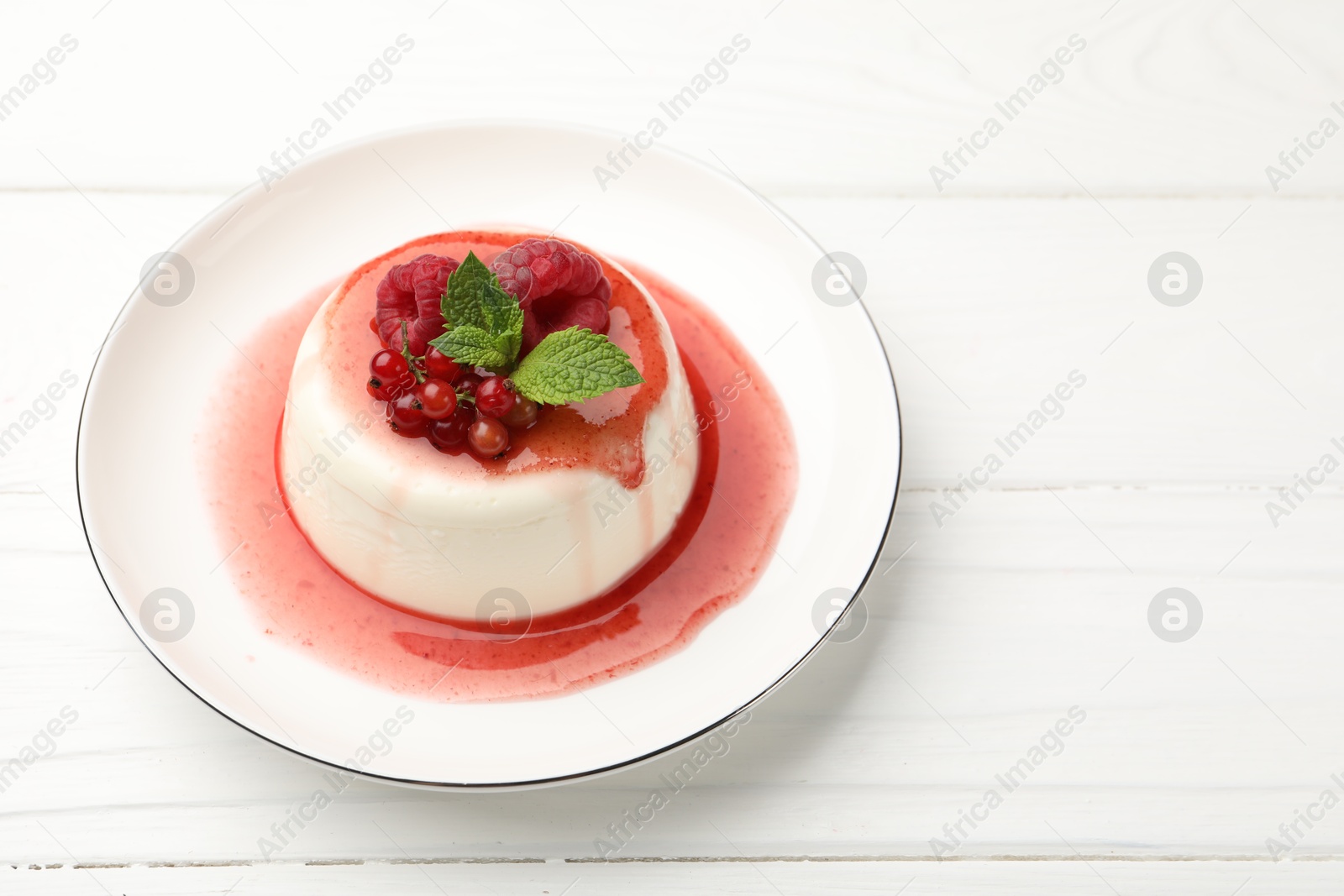 Delicious panna cotta with berries, sauce and mint on white wooden table, closeup Photo of Delicious panna cotta with berries, sauce and mint on white wooden table, closeup