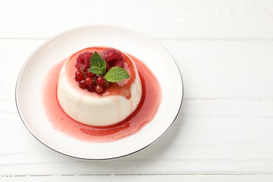 Photo of Delicious panna cotta with berries, sauce and mint on white wooden table, closeup