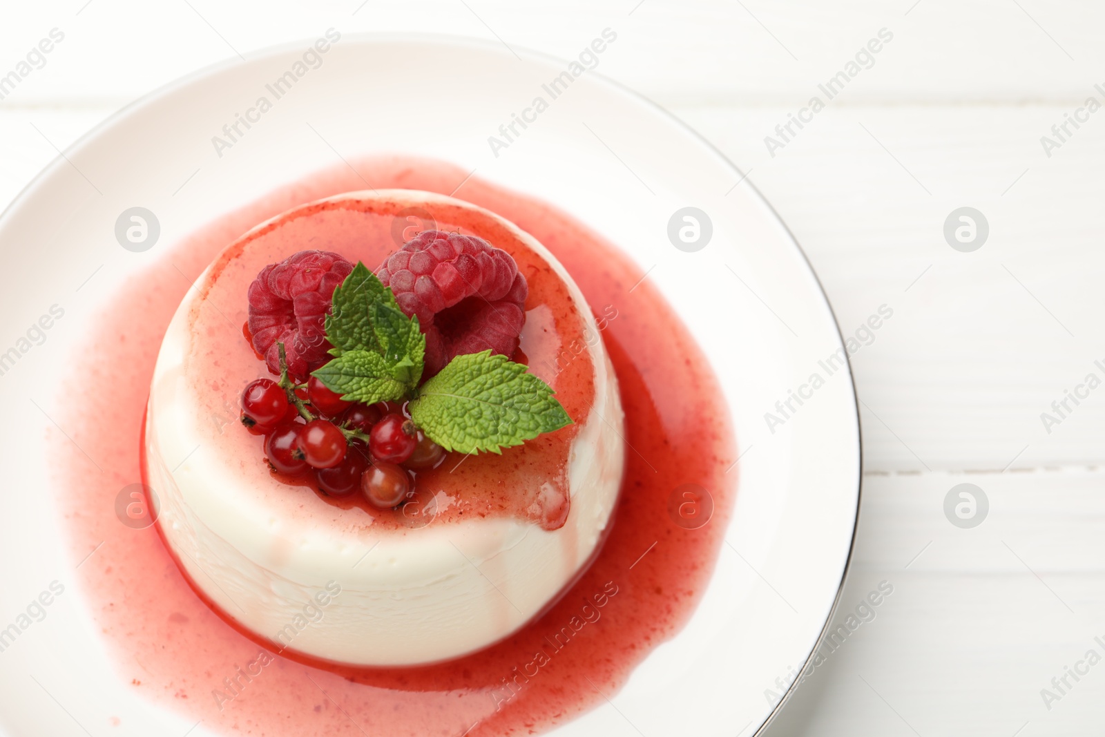 Delicious panna cotta with berries, sauce and mint on white wooden table, closeup Photo of Delicious panna cotta with berries, sauce and mint on white wooden table, closeup