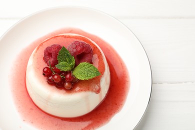 Photo of Delicious panna cotta with berries, sauce and mint on white wooden table, closeup
