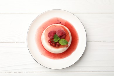 Photo of Delicious panna cotta with berries, sauce and mint on white wooden table, top view