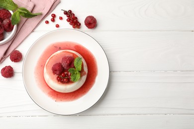 Photo of Delicious panna cotta with berries, sauce and mint on white wooden table, flat lay. Space for text