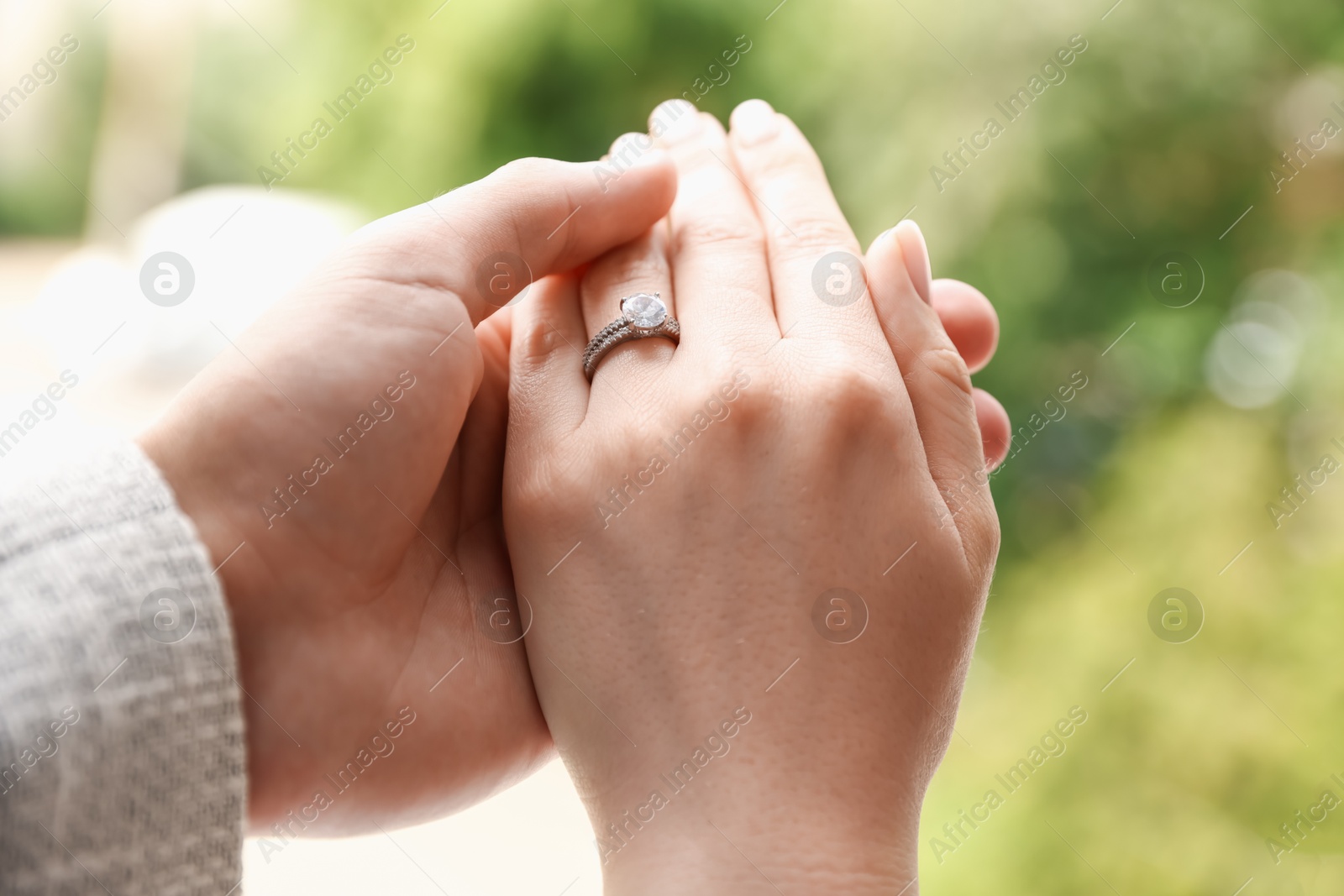 Photo of Making proposal. Woman with engagement ring and her fiance holding hands outdoors, closeup