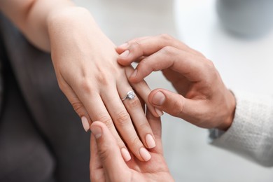 Photo of Making proposal. Man putting engagement ring on his girlfriend's finger indoors, closeup