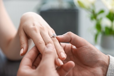 Photo of Making proposal. Man putting engagement ring on his girlfriend's finger indoors, closeup