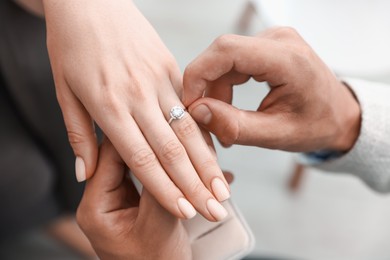 Photo of Making proposal. Man putting engagement ring on his girlfriend's finger indoors, above view