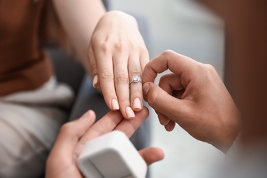 Photo of Making proposal. Man putting engagement ring on his girlfriend's finger indoors, closeup