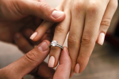 Photo of Making proposal. Man putting engagement ring on his girlfriend's finger indoors, closeup