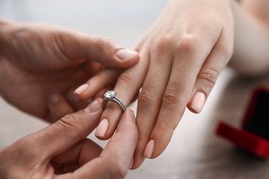 Photo of Making proposal. Man putting engagement ring on his girlfriend's finger indoors, closeup