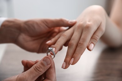 Photo of Making proposal. Man putting engagement ring on his girlfriend's finger indoors, closeup