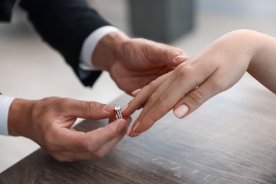 Photo of Making proposal. Man putting engagement ring on his girlfriend's finger indoors, closeup