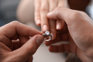 Photo of Making proposal. Man putting engagement ring on his girlfriend's finger indoors, closeup