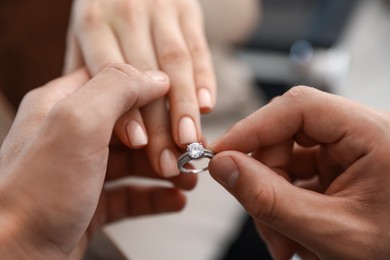 Photo of Making proposal. Man putting engagement ring on his girlfriend's finger indoors, closeup