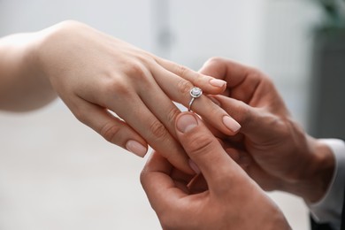 Photo of Making proposal. Man putting engagement ring on his girlfriend's finger indoors, closeup