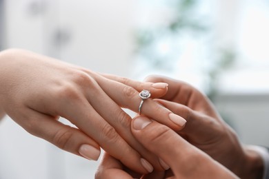 Photo of Making proposal. Man putting engagement ring on his girlfriend's finger indoors, closeup