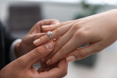Photo of Making proposal. Man putting engagement ring on his girlfriend's finger indoors, closeup