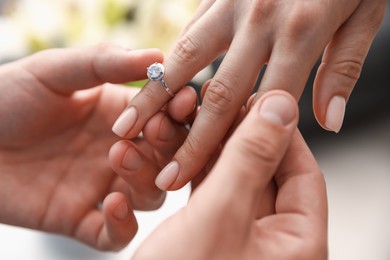 Photo of Making proposal. Man putting engagement ring on his girlfriend's finger indoors, closeup