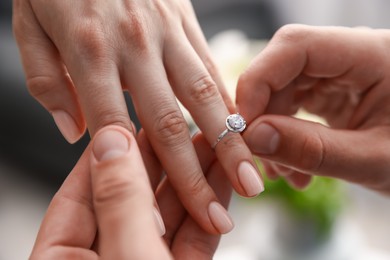Photo of Making proposal. Man putting engagement ring on his girlfriend's finger indoors, closeup