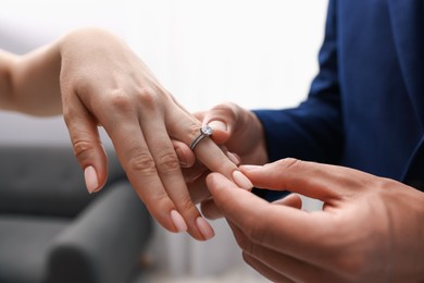 Photo of Making proposal. Man putting engagement ring on his girlfriend's finger indoors, closeup