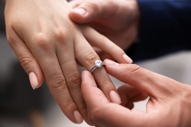 Photo of Making proposal. Man putting engagement ring on his girlfriend's finger indoors, closeup