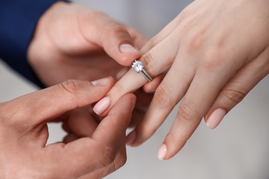 Photo of Making proposal. Man putting engagement ring on his girlfriend's finger indoors, closeup