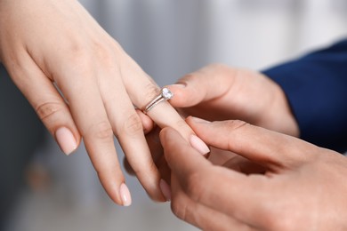 Photo of Making proposal. Man putting engagement ring on his girlfriend's finger indoors, closeup
