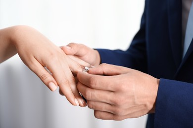 Photo of Making proposal. Man putting engagement ring on his girlfriend's finger indoors, closeup