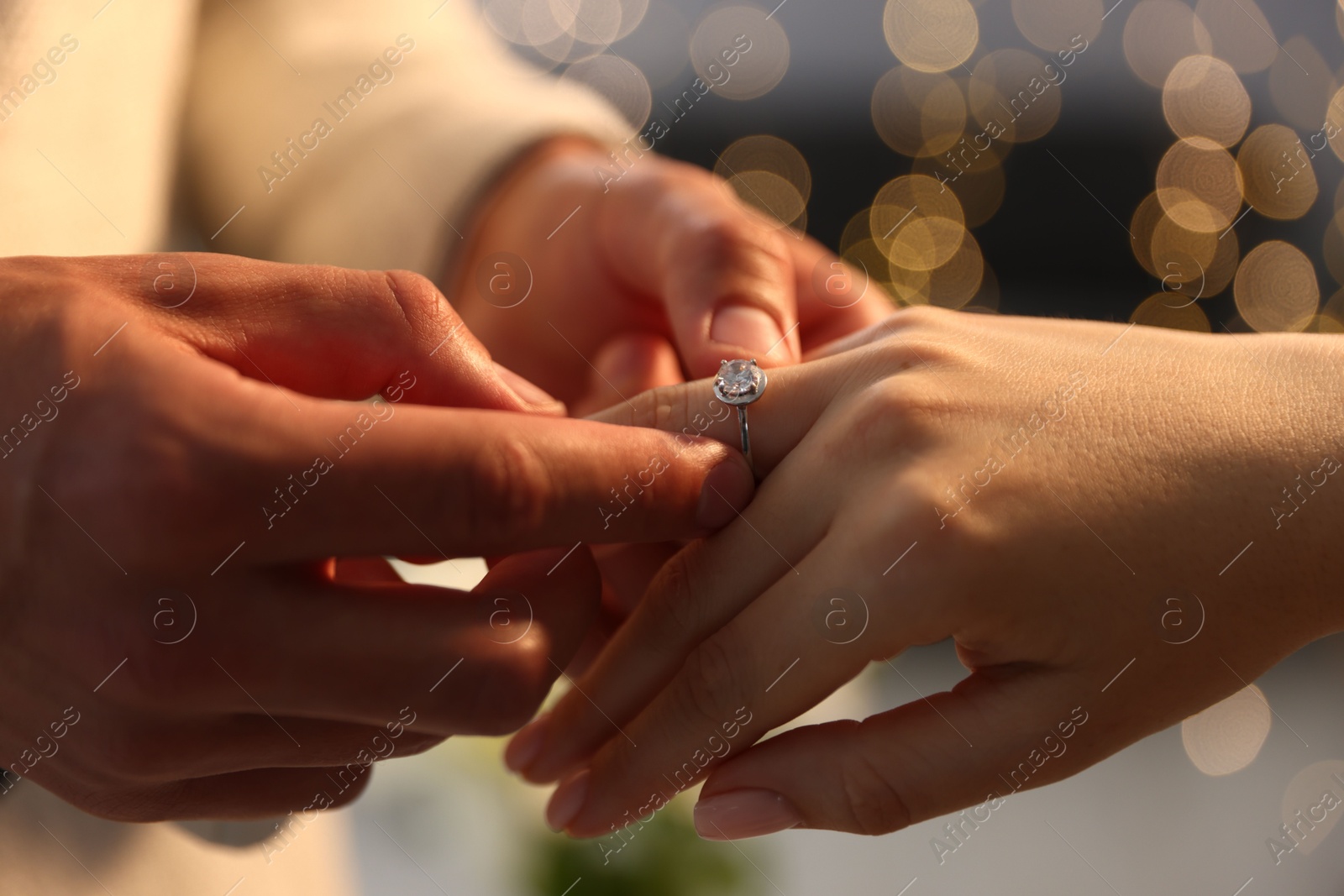 Making proposal. Man putting engagement ring on his girlfriend's finger indoors, closeup. Bokeh effect Photo of Making proposal. Man putting engagement ring on his girlfriend's finger indoors, closeup. Bokeh effect