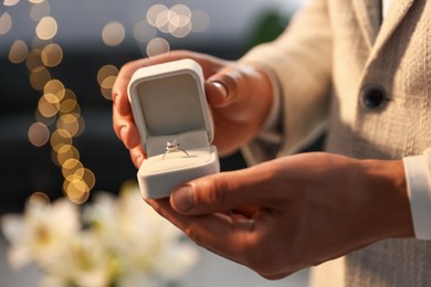 Photo of Making proposal. Man with engagement ring indoors, closeup. Bokeh effect