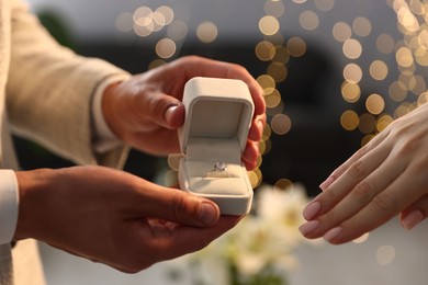 Photo of Man with engagement ring making marriage proposal to his girlfriend indoors, closeup. Bokeh effect