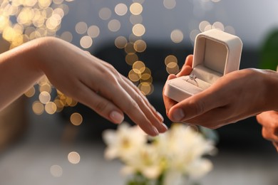 Photo of Man with engagement ring making marriage proposal to his girlfriend indoors, closeup. Bokeh effect