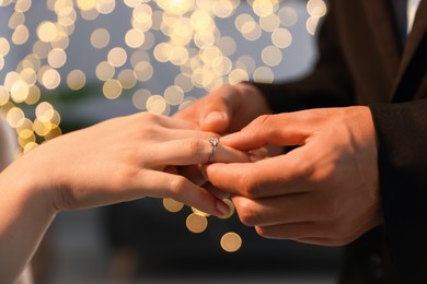 Photo of Making proposal. Man putting engagement ring on his girlfriend's finger indoors, closeup. Bokeh effect
