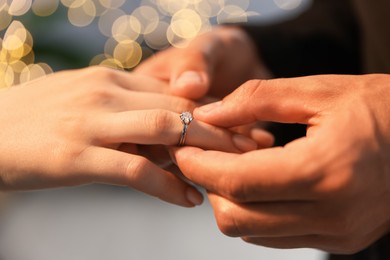 Photo of Making proposal. Man putting engagement ring on his girlfriend's finger indoors, closeup. Bokeh effect