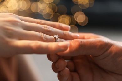 Photo of Making proposal. Man putting engagement ring on his girlfriend's finger indoors, closeup. Bokeh effect